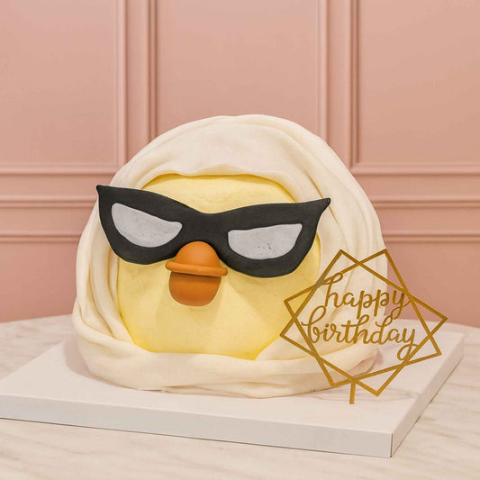 Cake shaped like a duck with sunglasses and 'Happy Birthday' decoration on a pink background