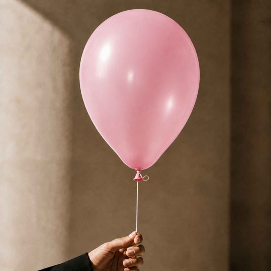 A single matte pink balloon held by a hand against a warm beige textured wall.