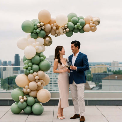 Couple standing in front of a colorful balloon arch on a rooftop with a cityscape background.