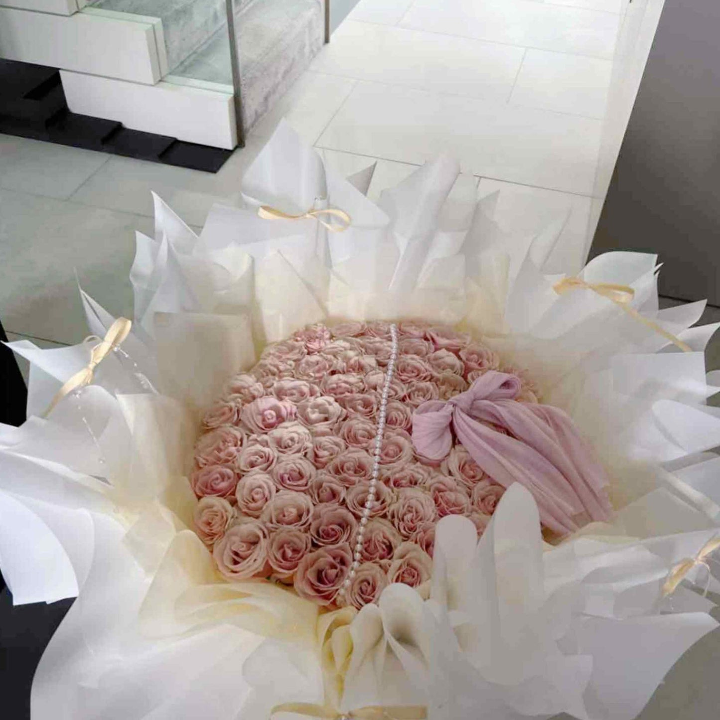Bouquet of pink roses with a pearl necklace and pink bow, wrapped in white paper.