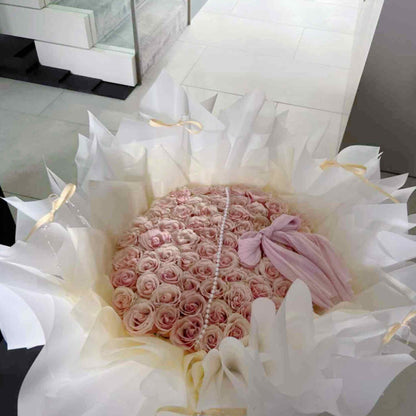 Bouquet of pink roses with a pearl necklace and pink bow, wrapped in white paper.