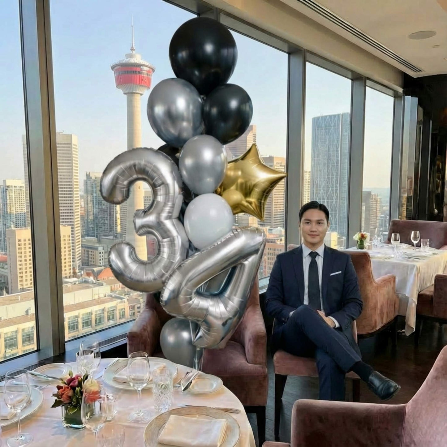 Man in a suit sitting at a table with balloons and a cityscape view