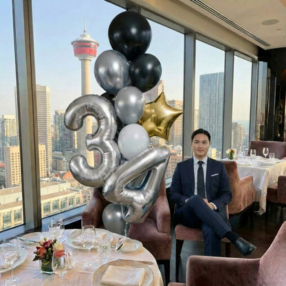 Man in a suit sitting at a table with balloons and a cityscape view