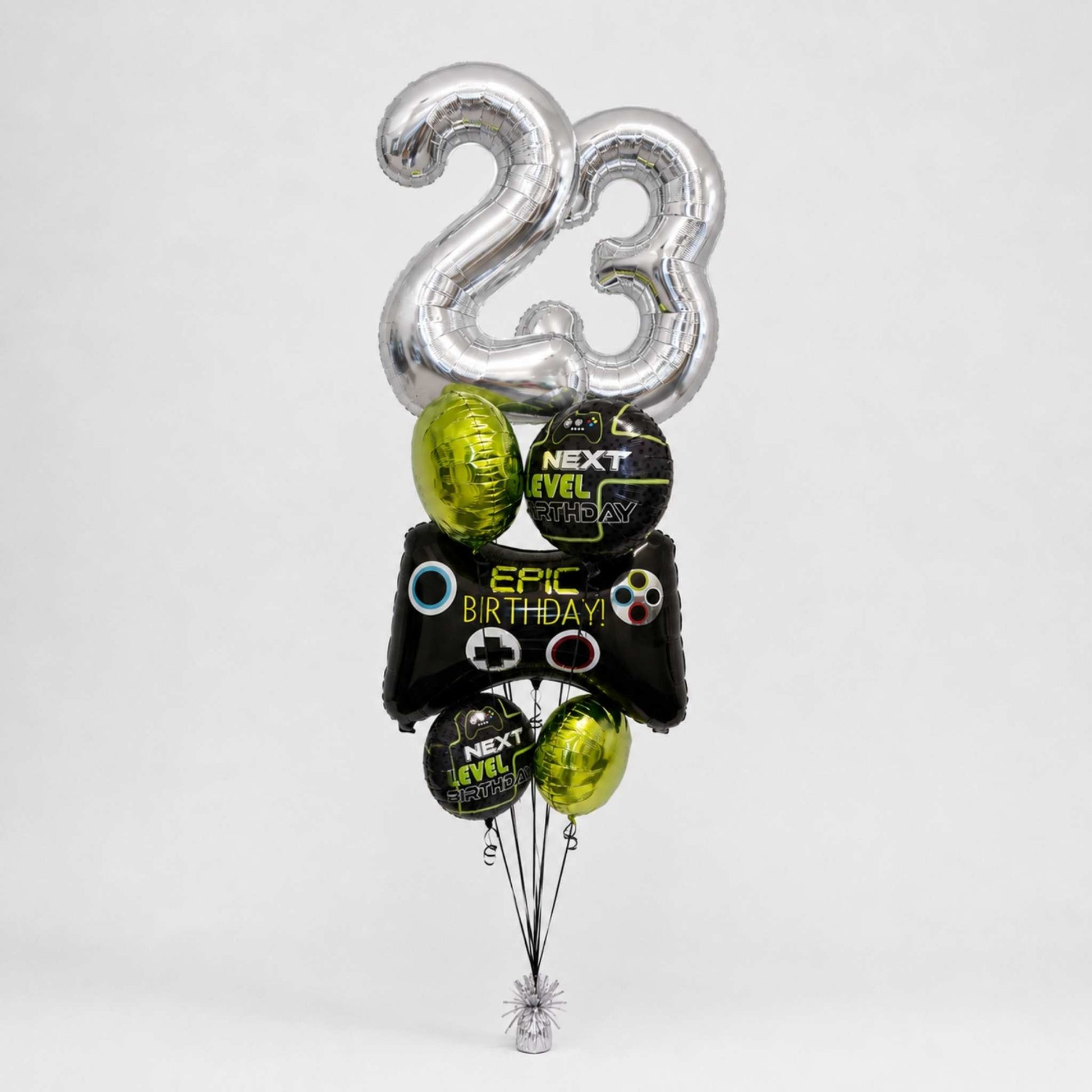 A balloon bouquet for a 23rd birthday featuring two large silver foil balloons shaped like the numbers '23', with several smaller black and metallic green balloons printed with video game controller graphics and the text 'EPIC BIRTHDAY' and 'NEXT LEVEL'.