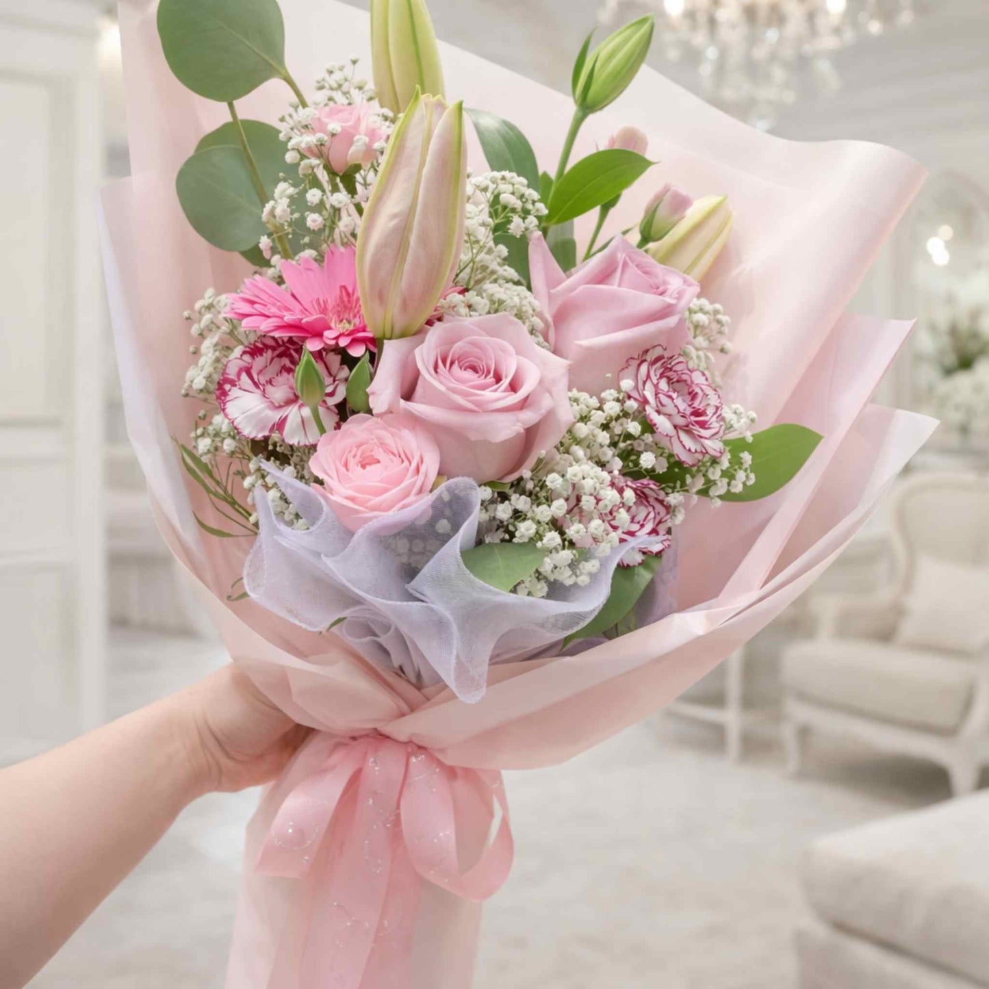 Bouquet of pink flowers with green leaves held by a hand, blurred indoor background