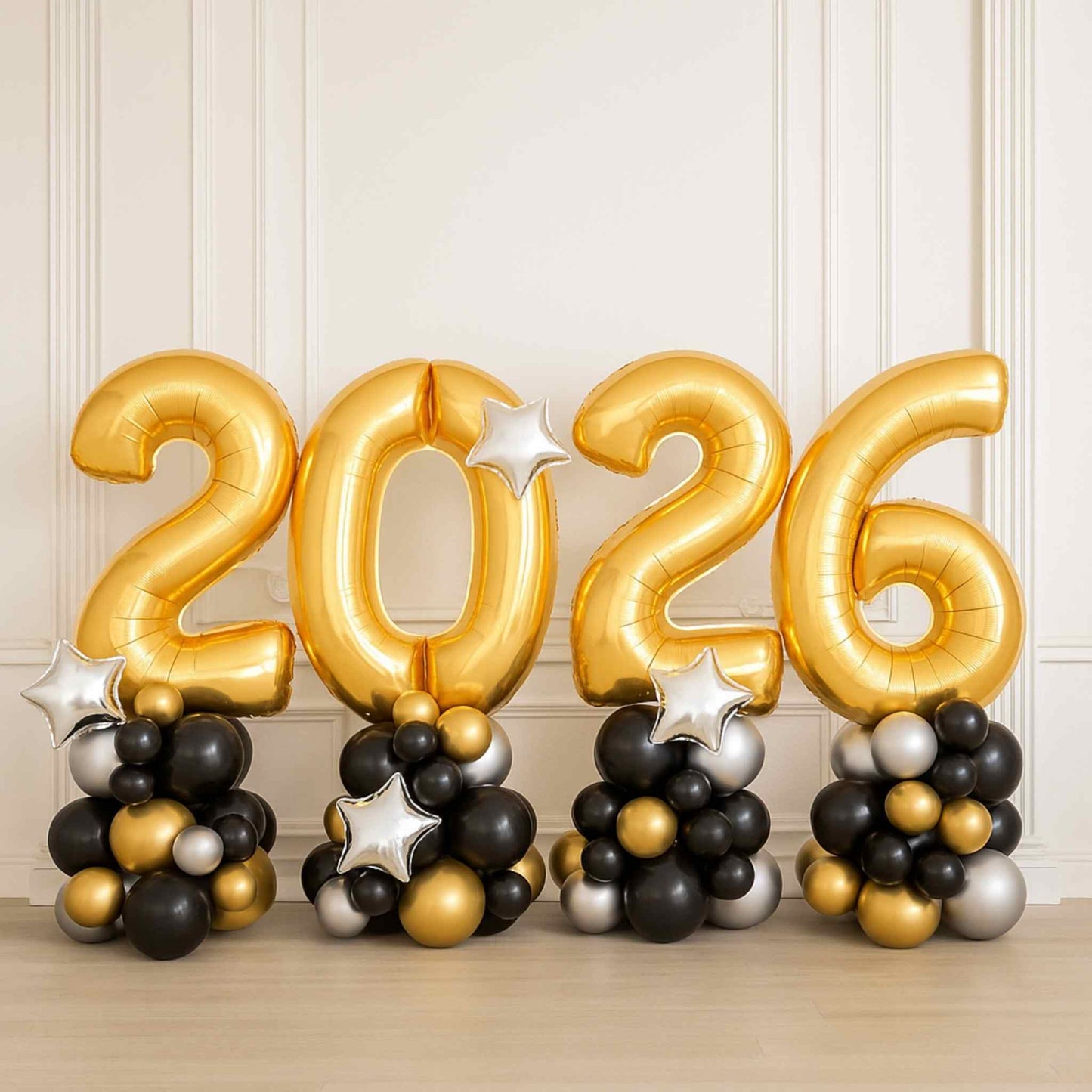 Gold '2026' balloons with black, silver, and gold balloons on a light wooden floor.