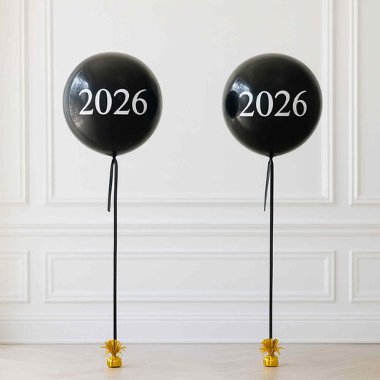 Two black balloons with '2026' printed on them against a white paneled wall.