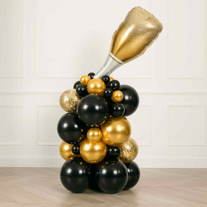 Balloon sculpture of a champagne bottle with black and gold balloons on a light wooden floor.