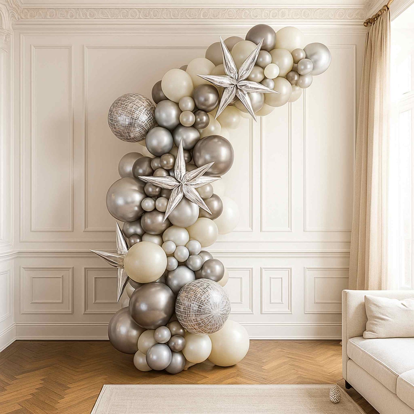 Balloon arch with silver and white balloons in a room with a couch and window.