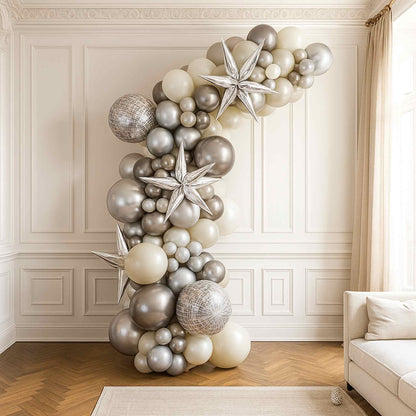 Balloon arch with silver and white balloons in a room with a couch and window.