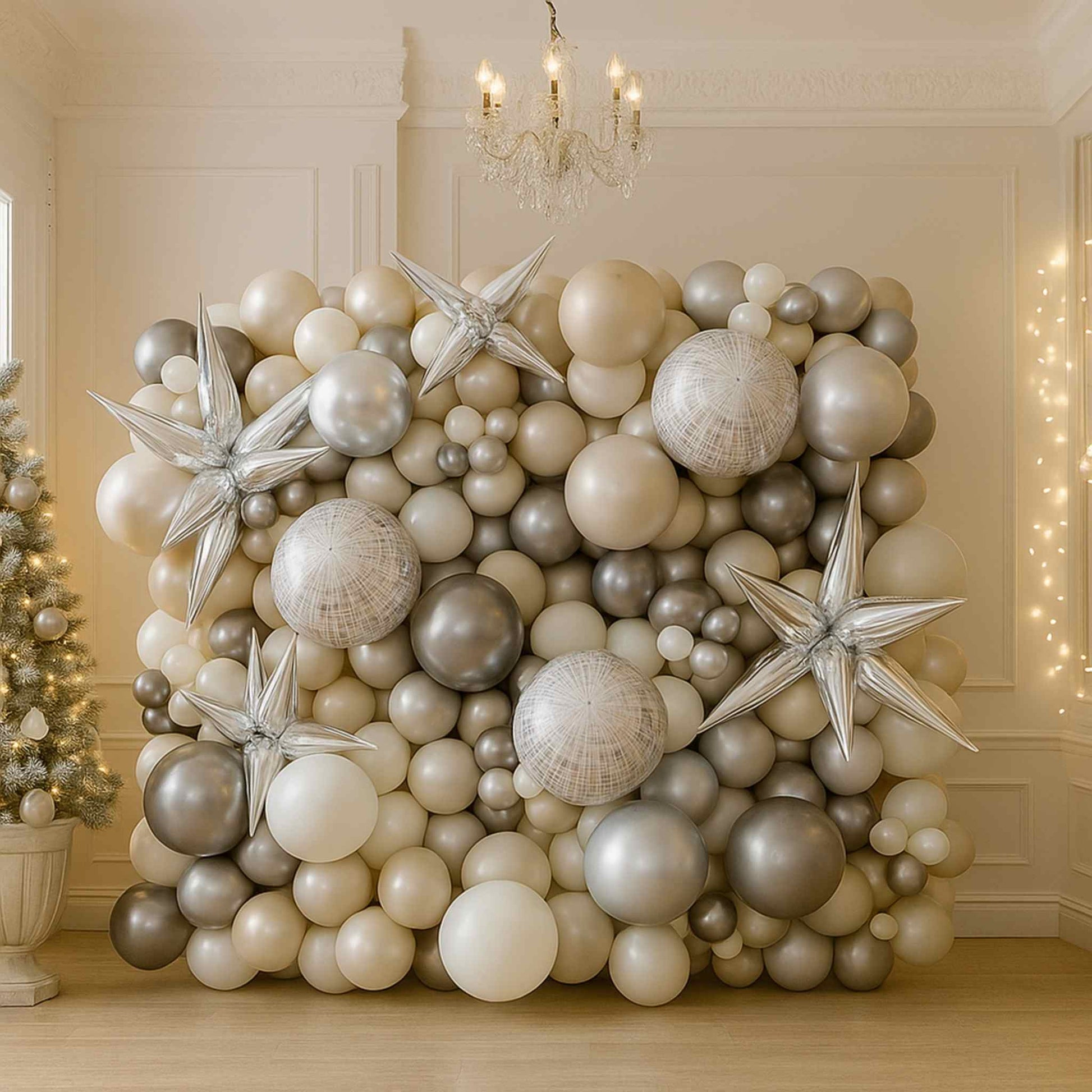 Decorative balloon wall with silver and white balloons in a room with a chandelier and Christmas tree.