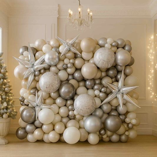 Decorative balloon wall with silver and white balloons in a room with a chandelier and Christmas tree.
