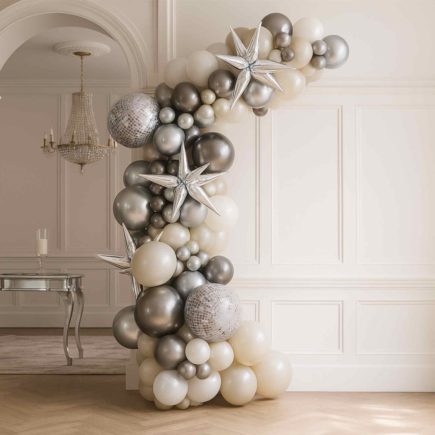 Balloon arch with silver, gray, and white balloons in a room with a chandelier.