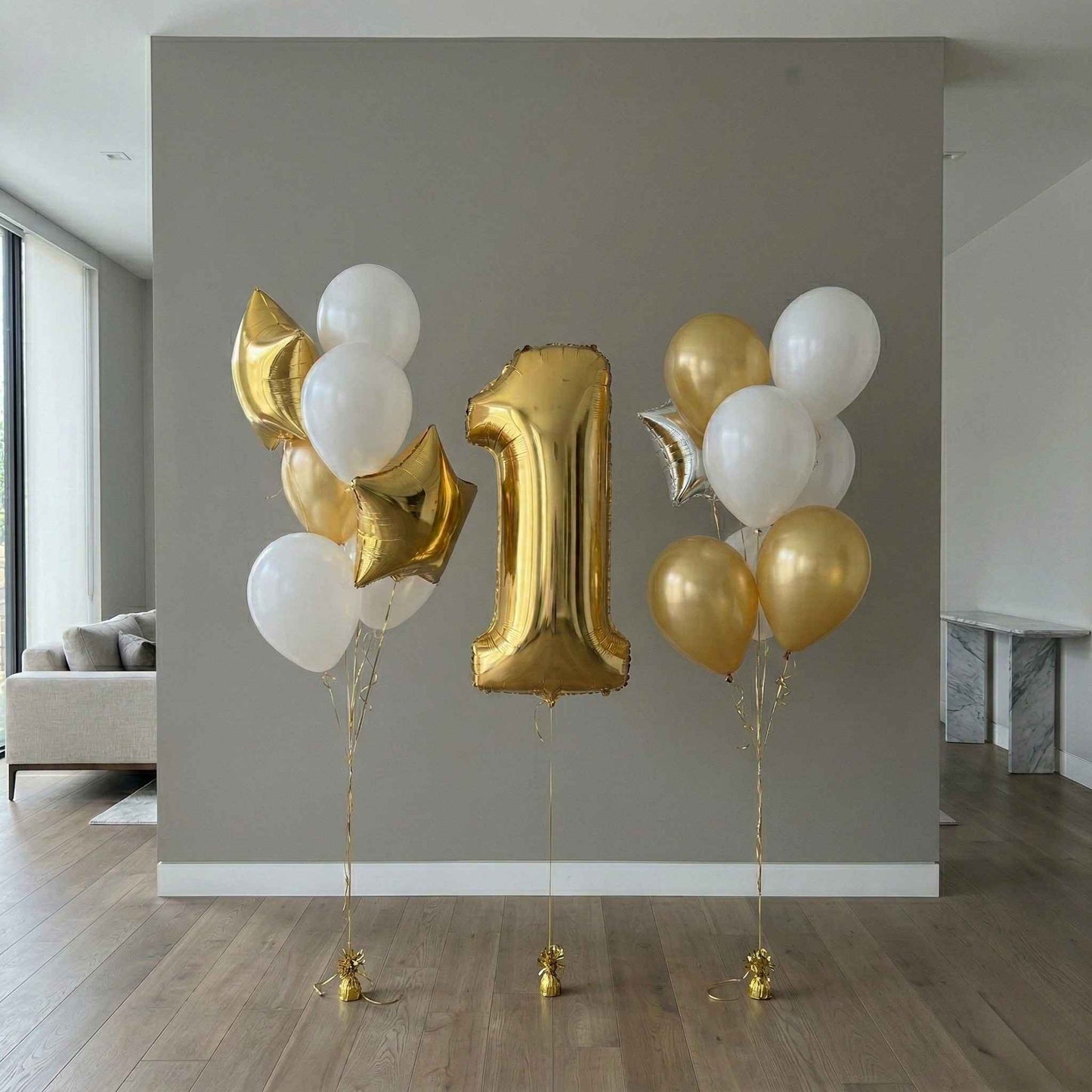Gold and white balloons with a number 1 balloon against a gray wall.
