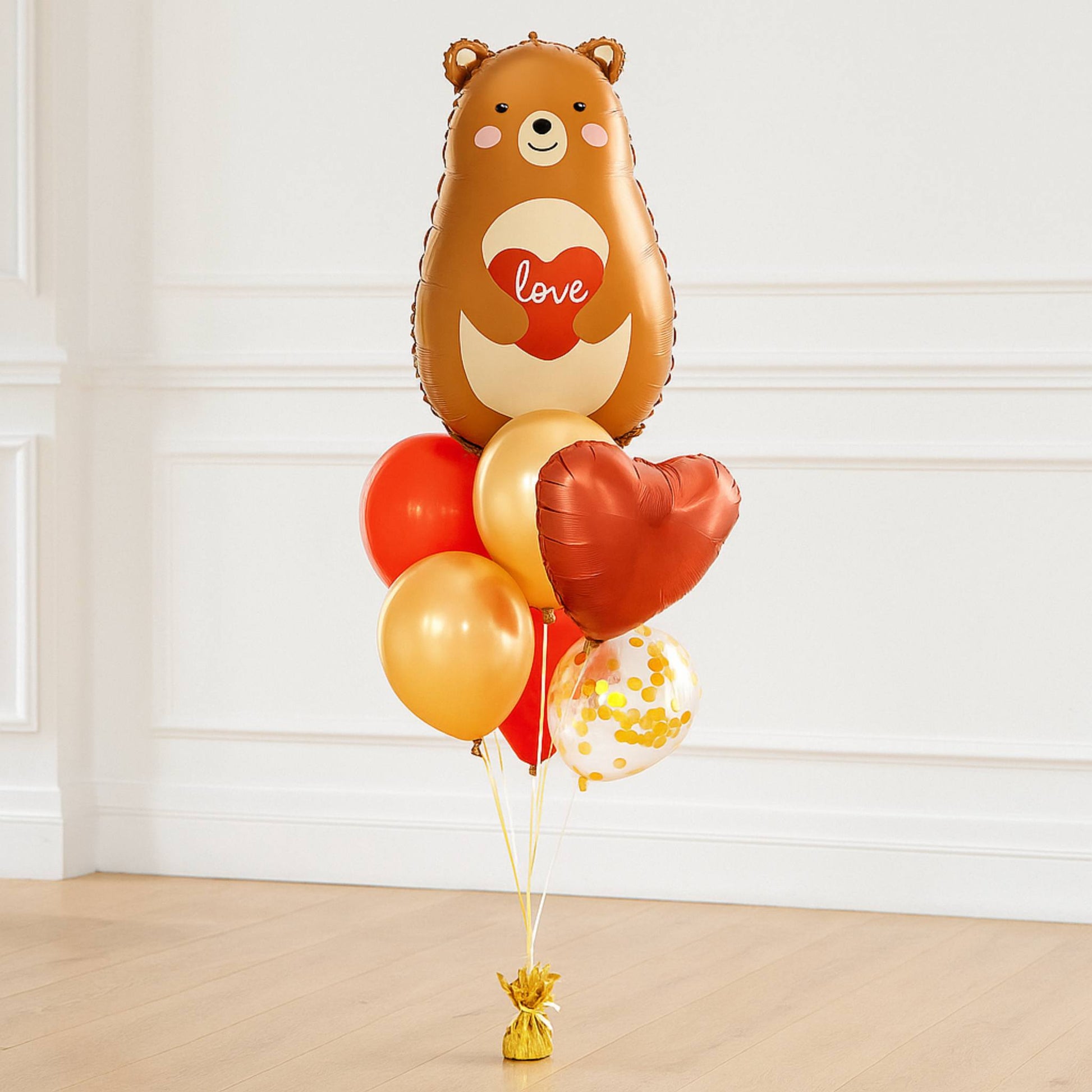 Balloon bouquet with a bear-shaped balloon and heart designs on a light wooden floor.
