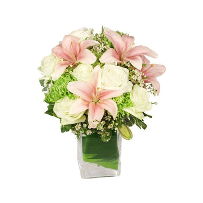 A floral arrangement featuring pale pink lilies, pale green roses, and lime-green spider mums in a rectangular clear vase with green foliage.