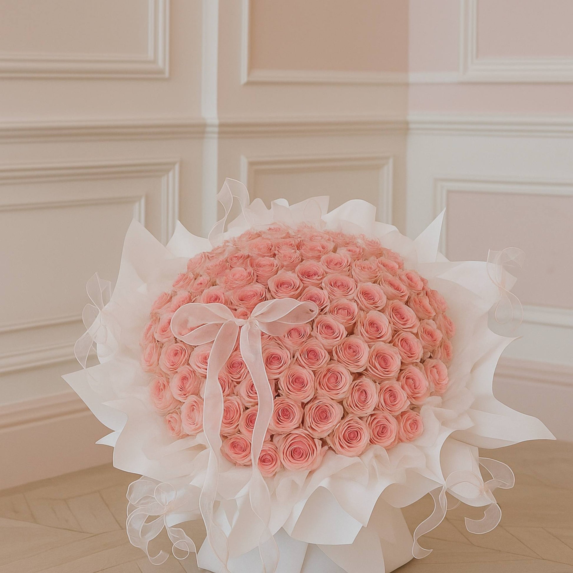 Bouquet of pink roses with white ribbons on a light wooden floor.