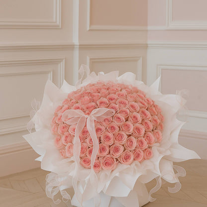 Bouquet of pink roses with white ribbons on a light wooden floor.