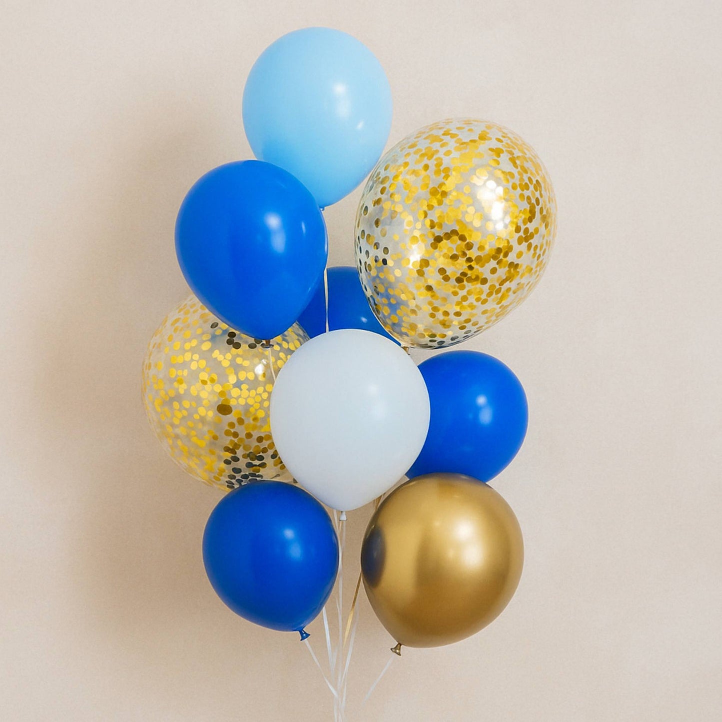 Bouquet of balloons in blue, gold, and white with confetti on a beige background