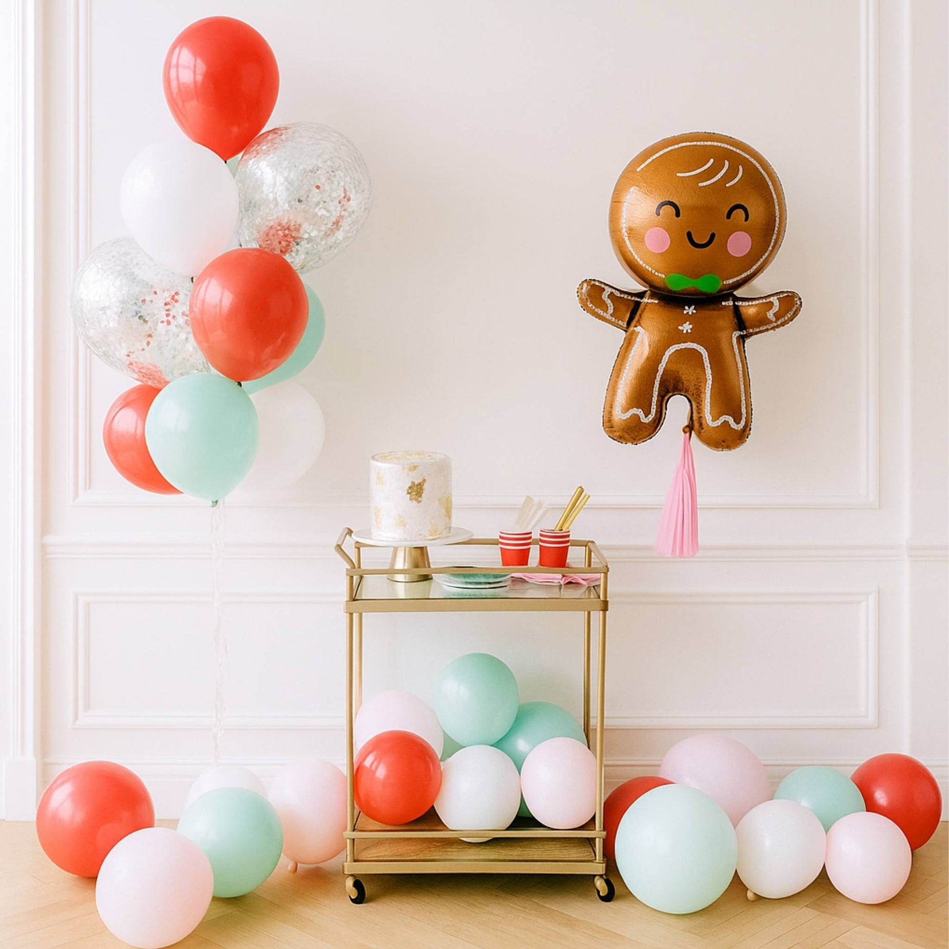 Decorative setup with colorful balloons and a gingerbread man balloon on a white wall.