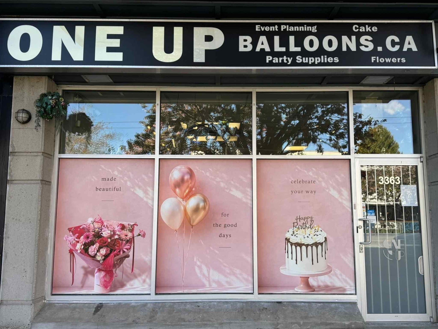  storefront with 'ONE UP BALLOONS.CA' sign and window displays of balloons, flowers, and cake.
