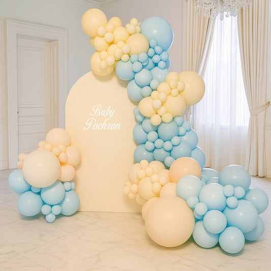 Balloon arch with blue and yellow balloons in a room with white walls and curtains.