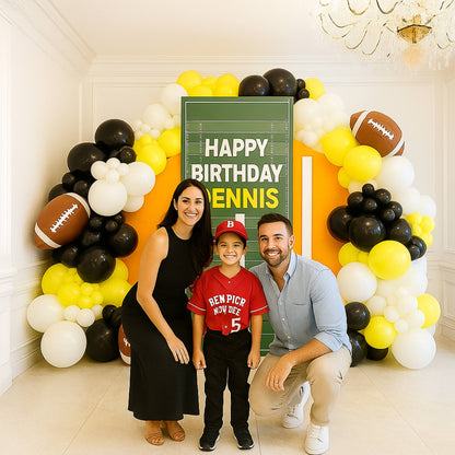 Family posing in front of a 'Happy Birthday Dennis' sign with a balloon arch.
