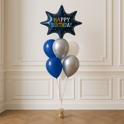 A bouquet of balloons featuring a 27-inch helium-filled Happy Birthday Blast foil balloon in blue and gold, accompanied by two smaller balloons in blue and white, all arranged with white curling ribbon against a wall.