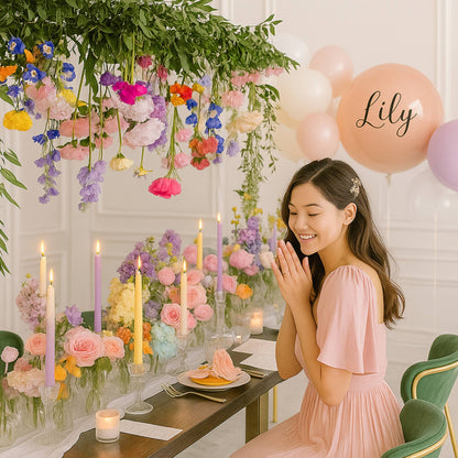 Woman in a pink dress sitting at a decorated table with flowers and candles, surrounded by balloons.