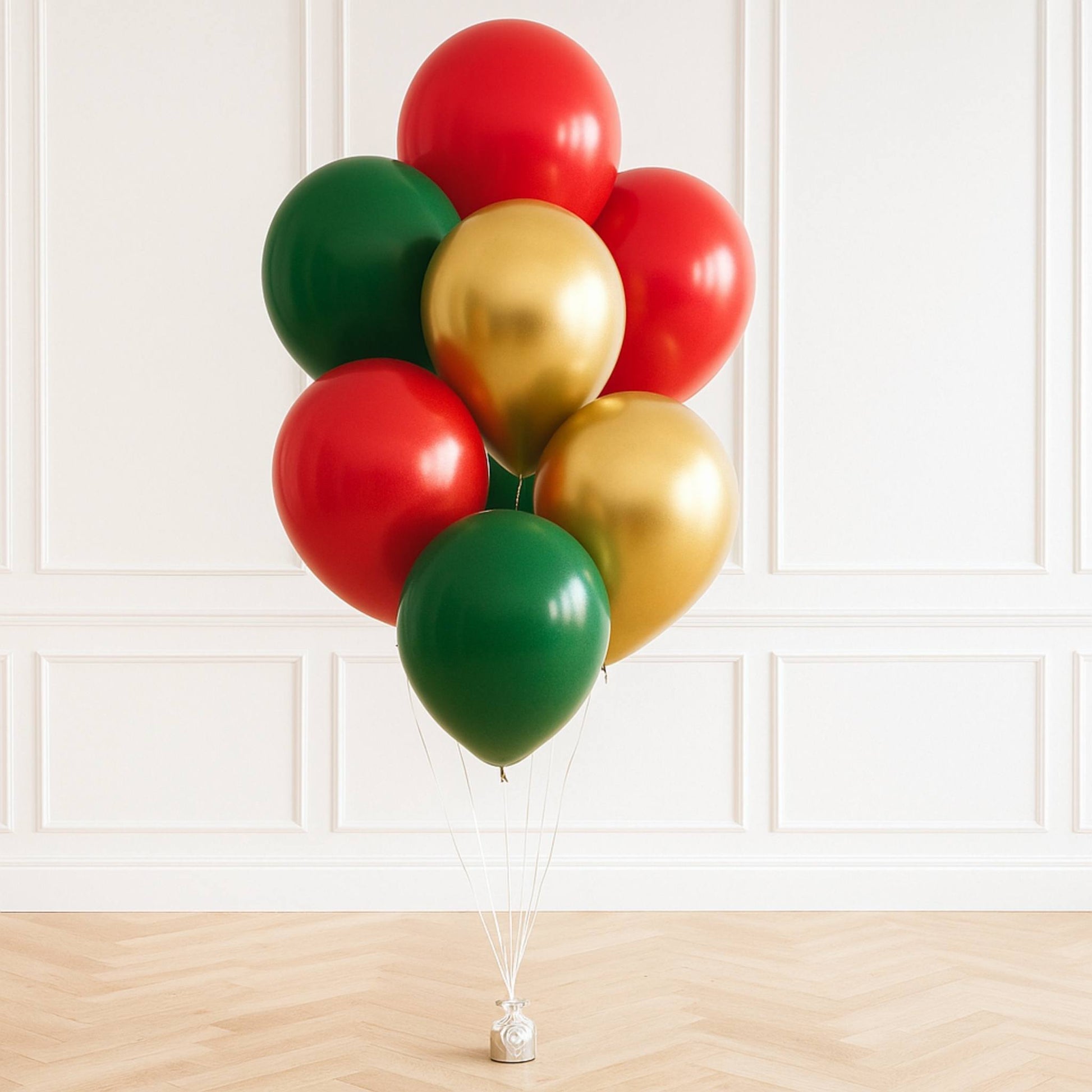 Bunch of red, green, and gold balloons tied together against a white paneled wall.