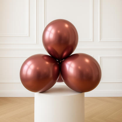 Three rose gold balloons on a white pedestal against a white paneled wall.