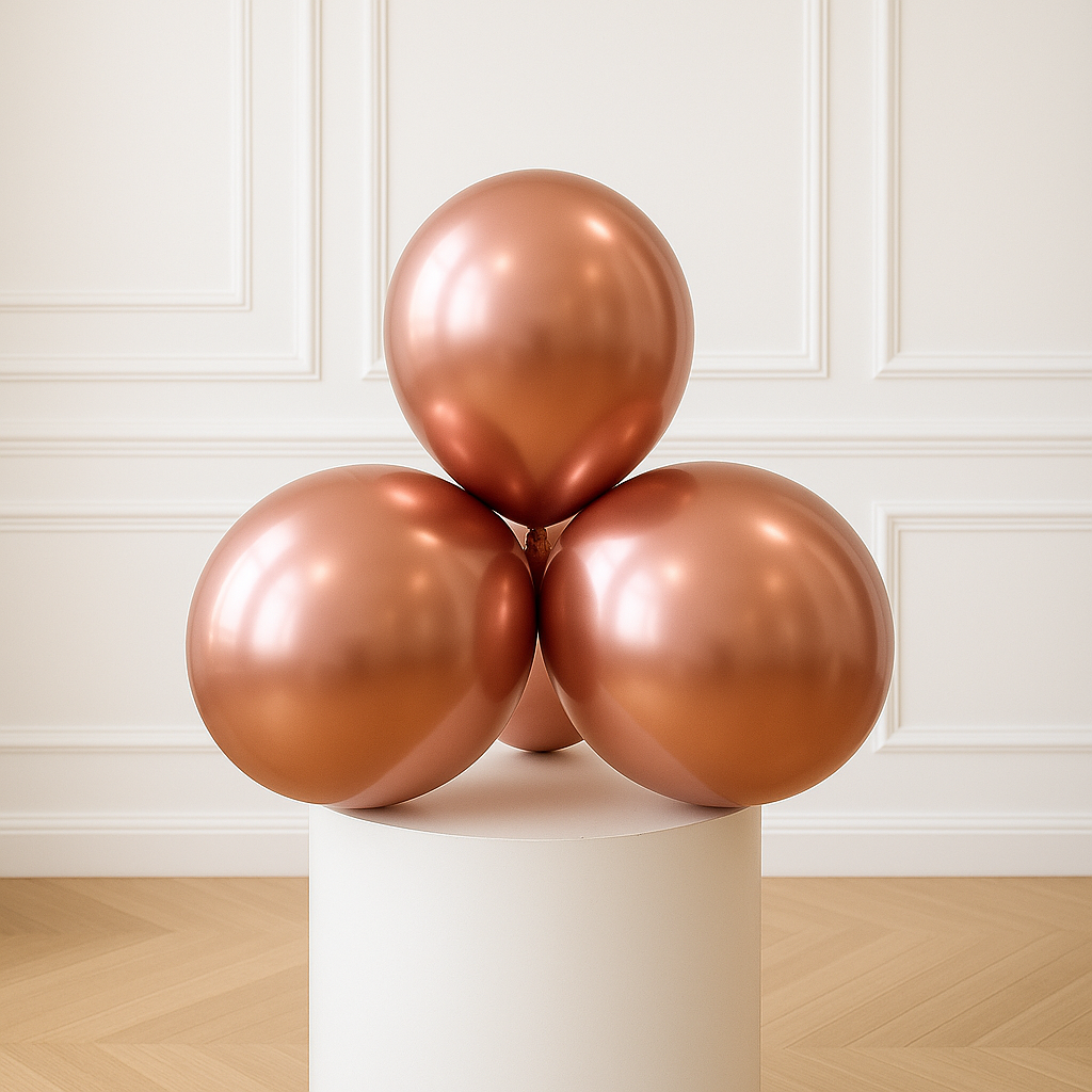 Three rose gold balloons stacked on a white pedestal against a white paneled wall.