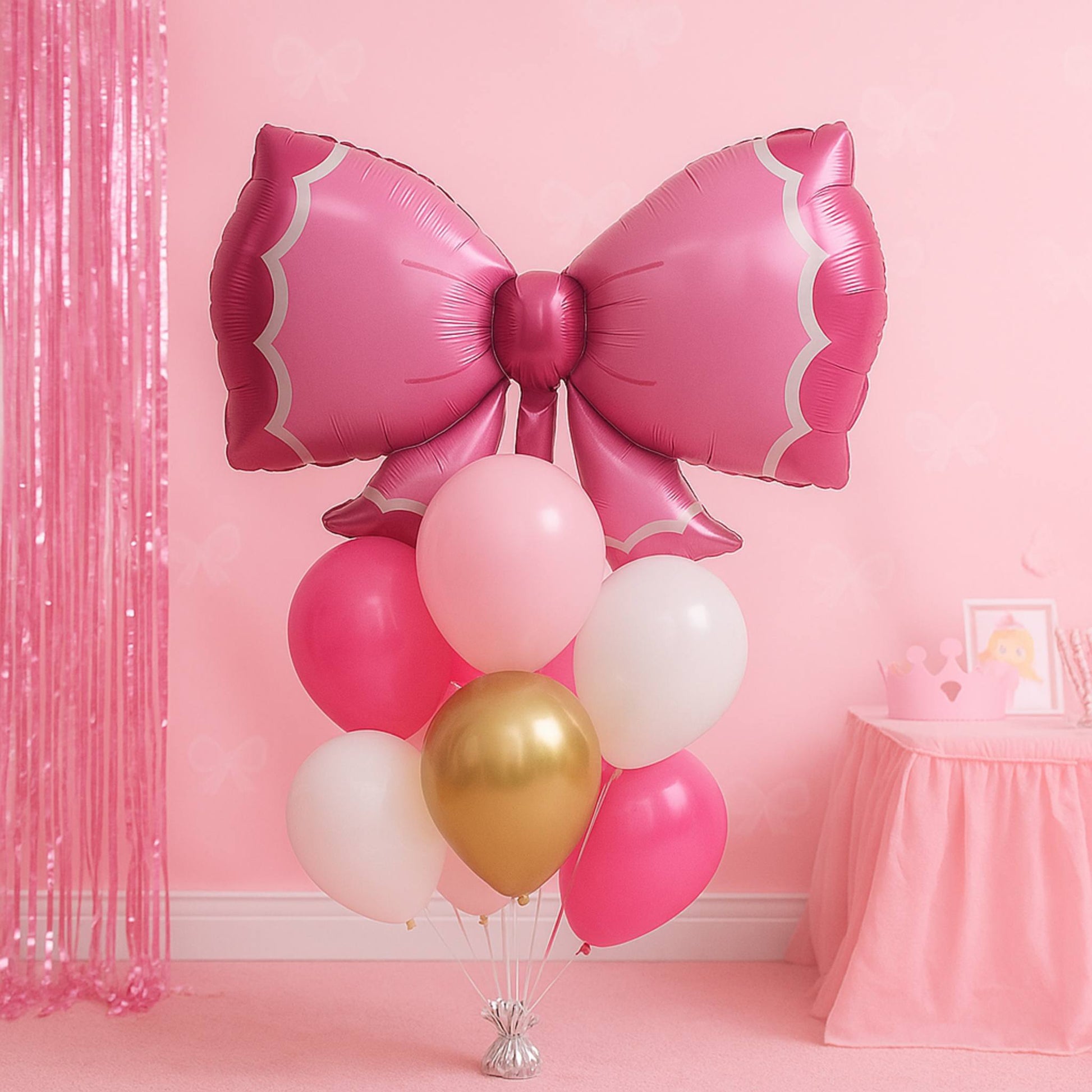 Pink bow-shaped balloon with other balloons against a pink wall