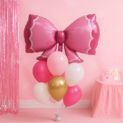Pink bow-shaped balloon with other balloons against a pink wall