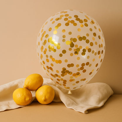 Clear balloon with gold confetti next to three lemons on a beige surface