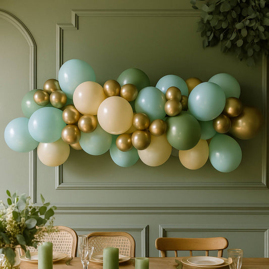 Balloon garland in green, gold, and beige hanging on a green wall above a dining table.