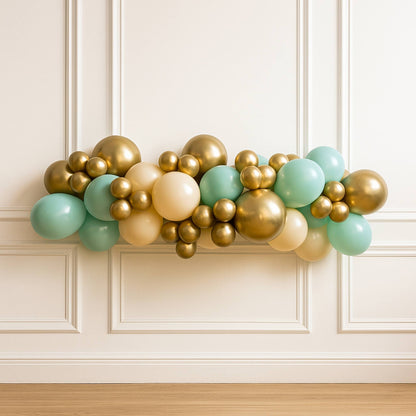 Balloon garland with gold, green, and beige balloons against a white paneled wall.