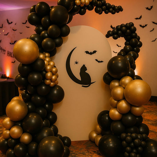 Halloween-themed balloon arch with black and gold balloons, a ghost, and bats on a white board.