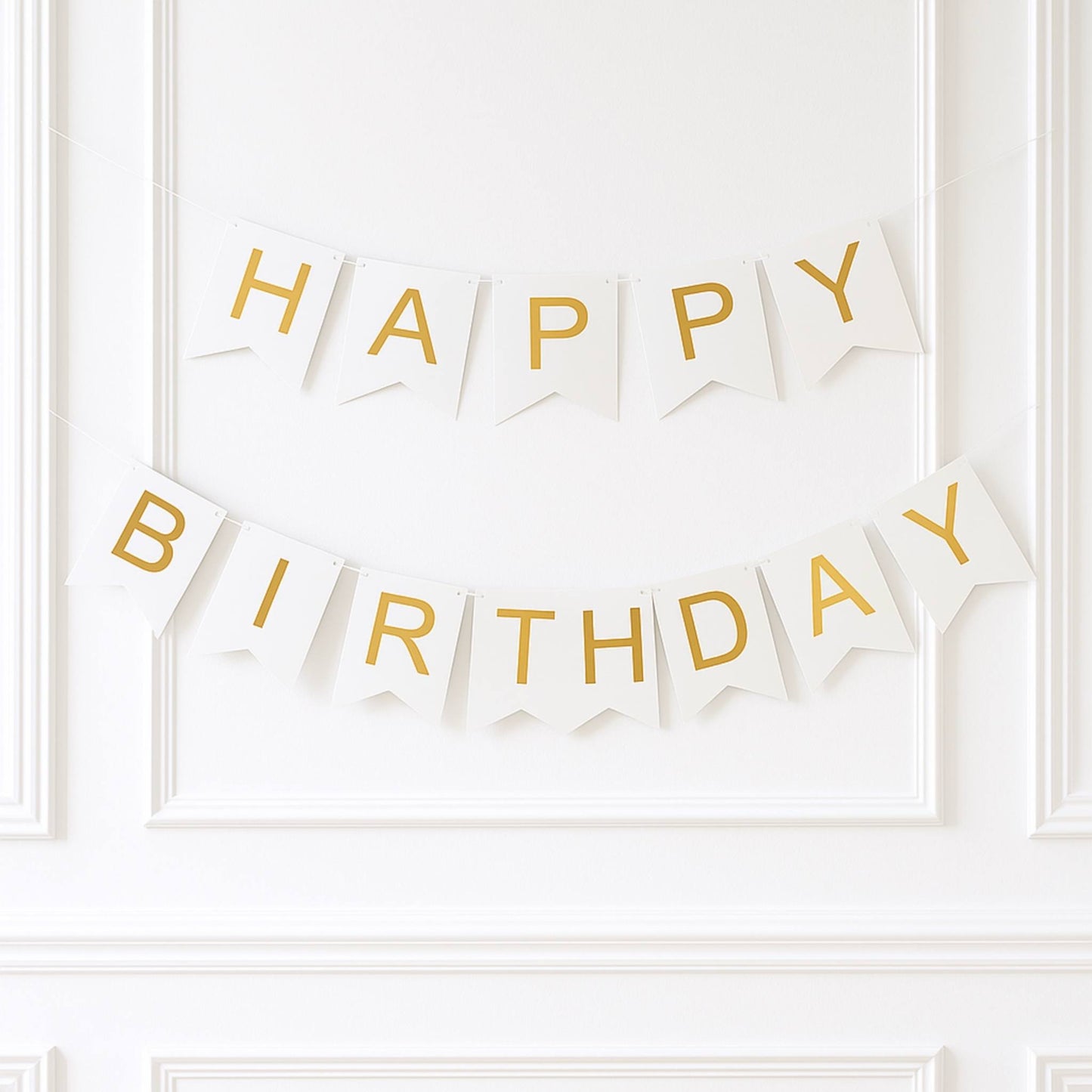 White and gold 'Happy Birthday' banner on a white wall.