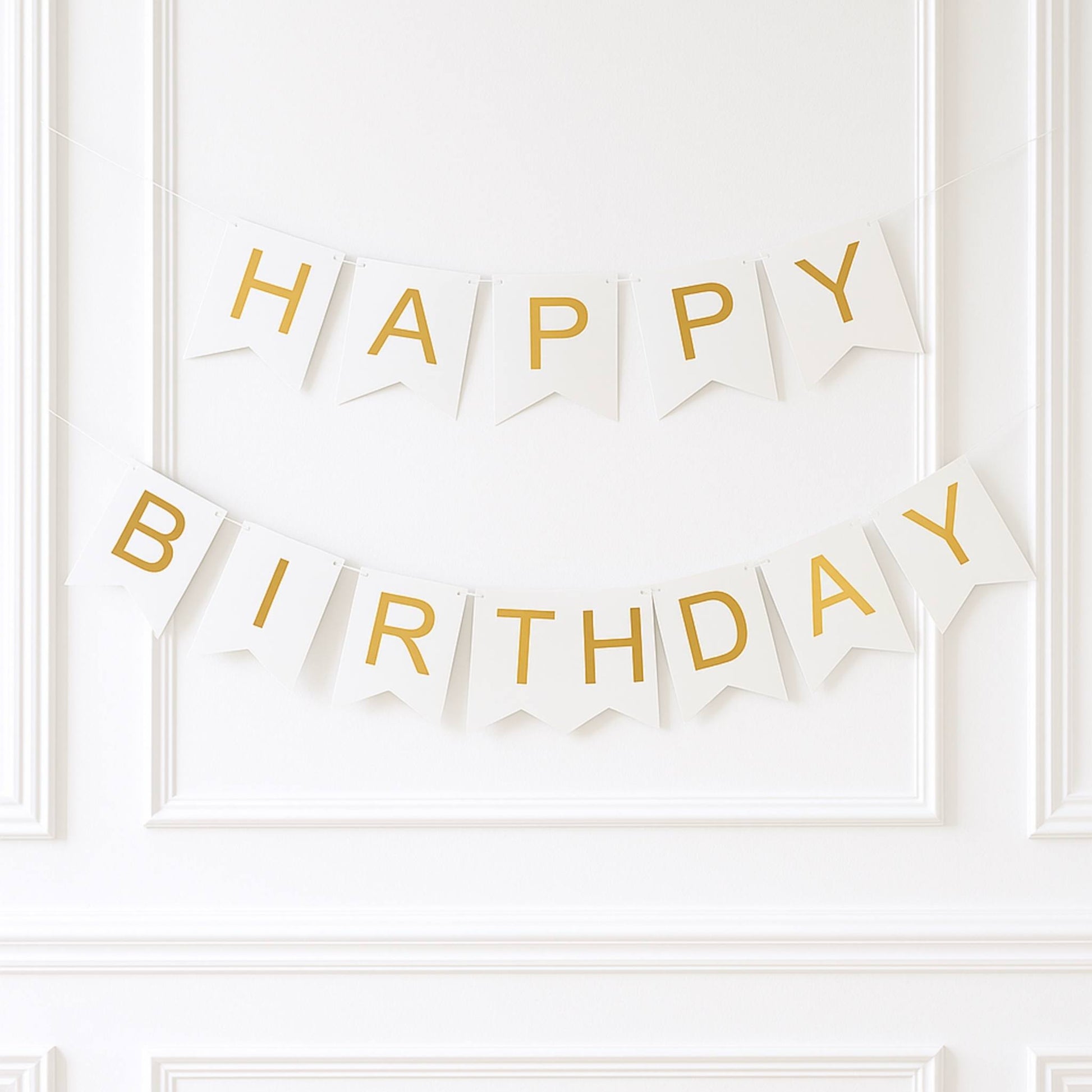 White and gold 'Happy Birthday' banner on a white wall.