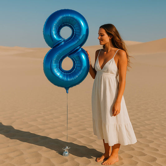 Woman in a white dress holding a large blue number 8 balloon in a desert setting