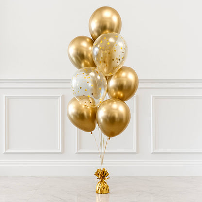 Bouquet of gold and clear balloons with gold confetti against a white wall.