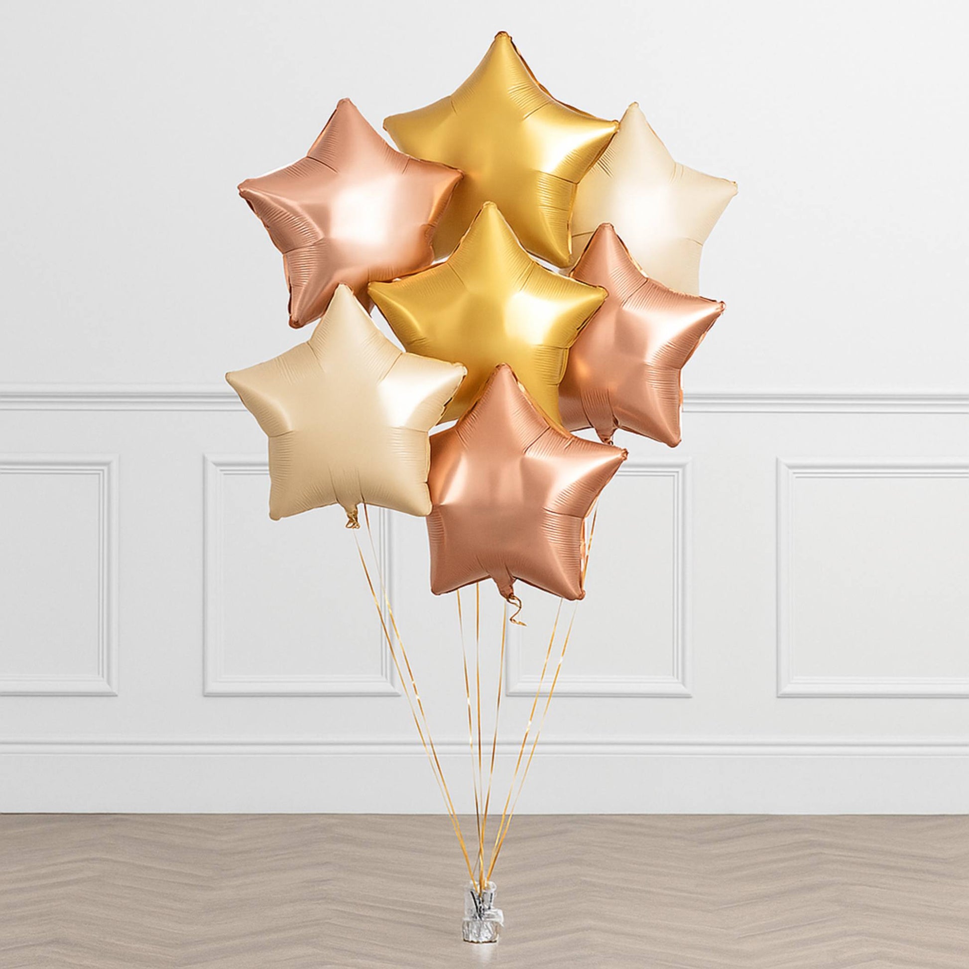 Bouquet of star-shaped balloons in gold, rose gold, and beige on a white paneled wall background.