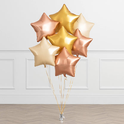 Bouquet of star-shaped balloons in gold, rose gold, and beige on a white paneled wall background.