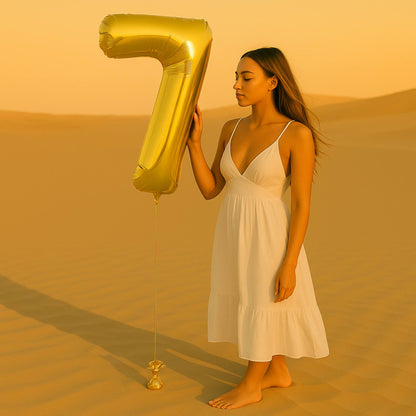 Woman in a white dress holding a large gold number 7 balloon in a desert setting