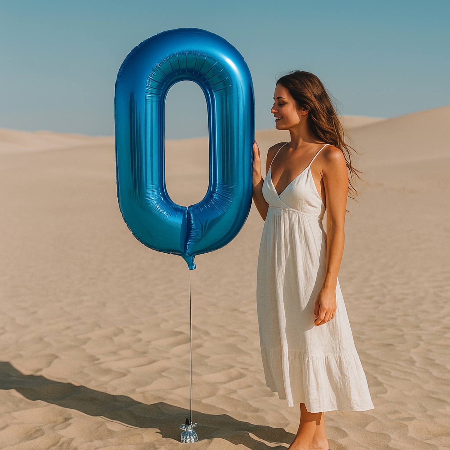 Woman holding a large blue number '0' balloon in a desert setting