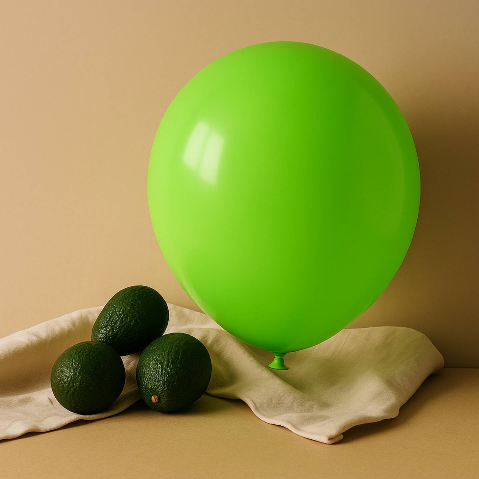 Green 11 inch helium balloon and avocados on a beige surface with a beige background