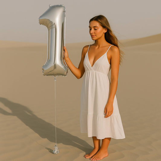 Woman in a white dress holding a large silver number '1' balloon in a desert setting