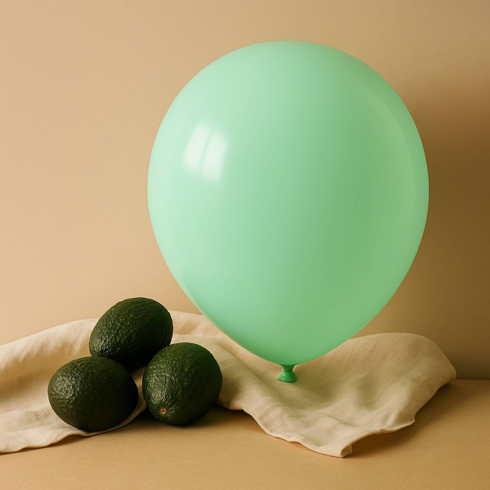 mint 11 inch helium balloon and avocados on a beige cloth against a beige background