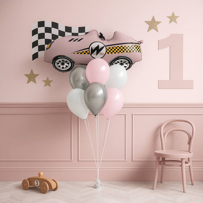 Pink car-shaped balloon with balloons in a room with a pink wall, chair, and small wooden toy car.
